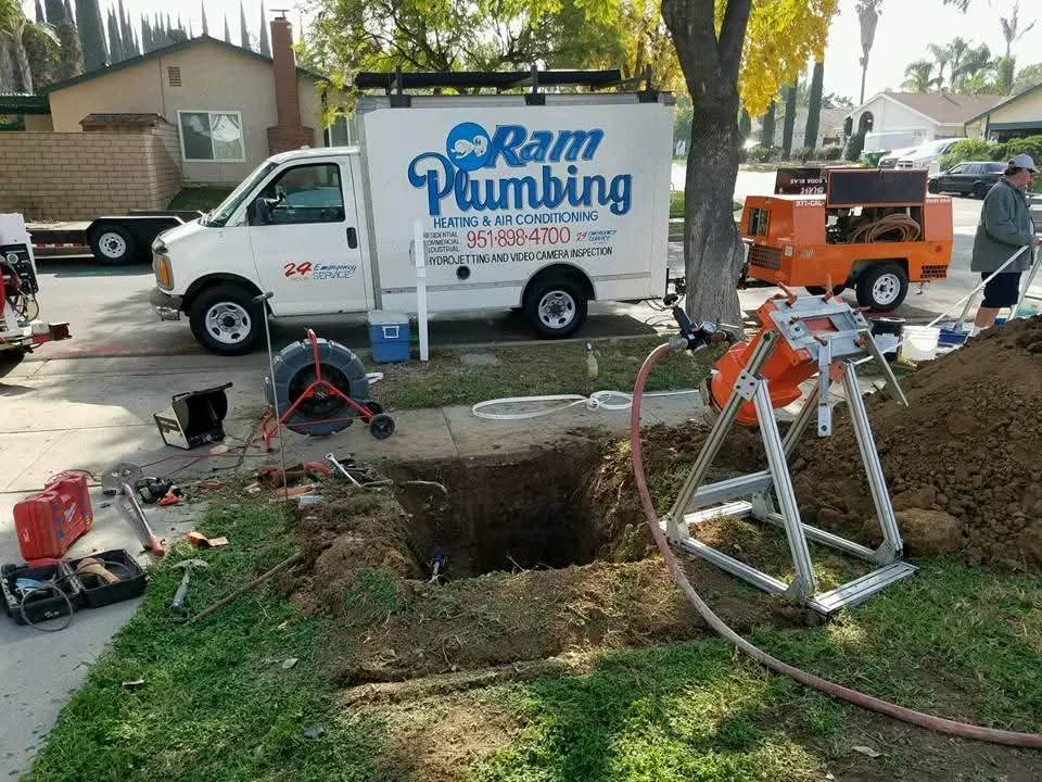 Sewer line excavation with exposed main line, trench work, and professional plumbing equipment on site
