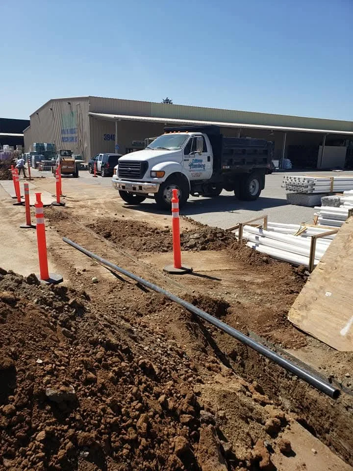 Underground PVC pipe installation with trenching, safety bollards, and staged materials on commercial site