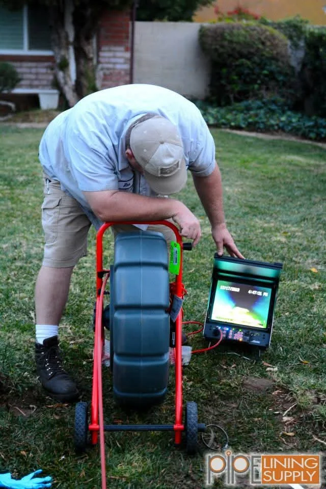 Technician operating motorized sewer camera reel with monitor displaying underground pipe inspection footage