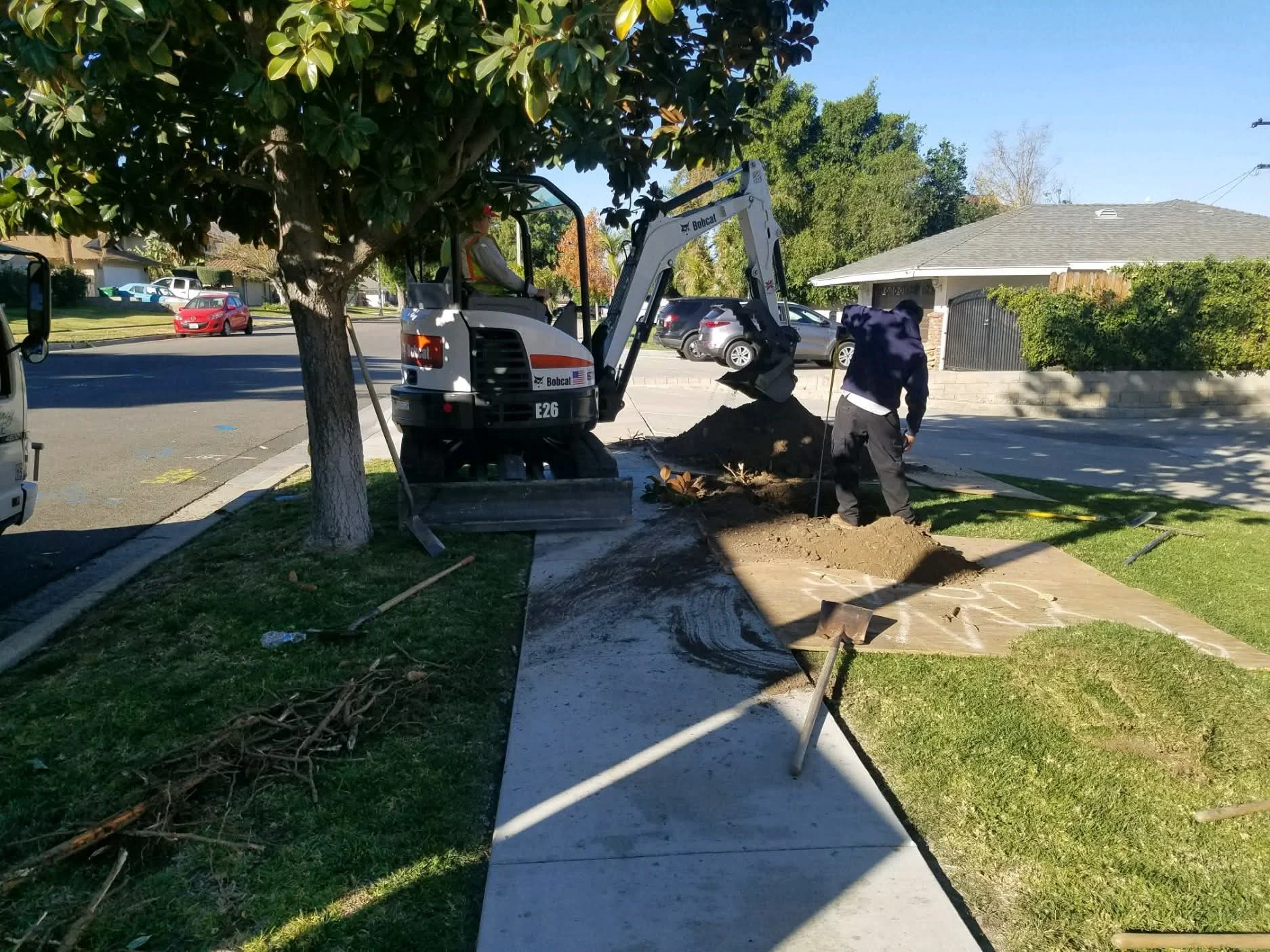 Bobcat excavator removing soil for underground utility access in residential yard