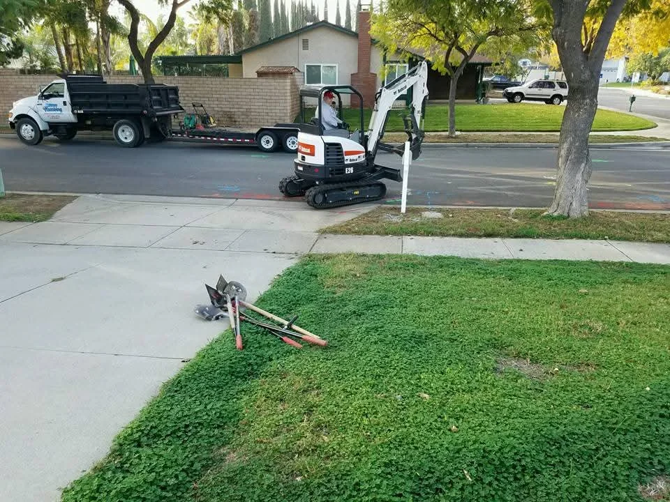 Mini excavator and dump truck on residential driveway during utility excavation work