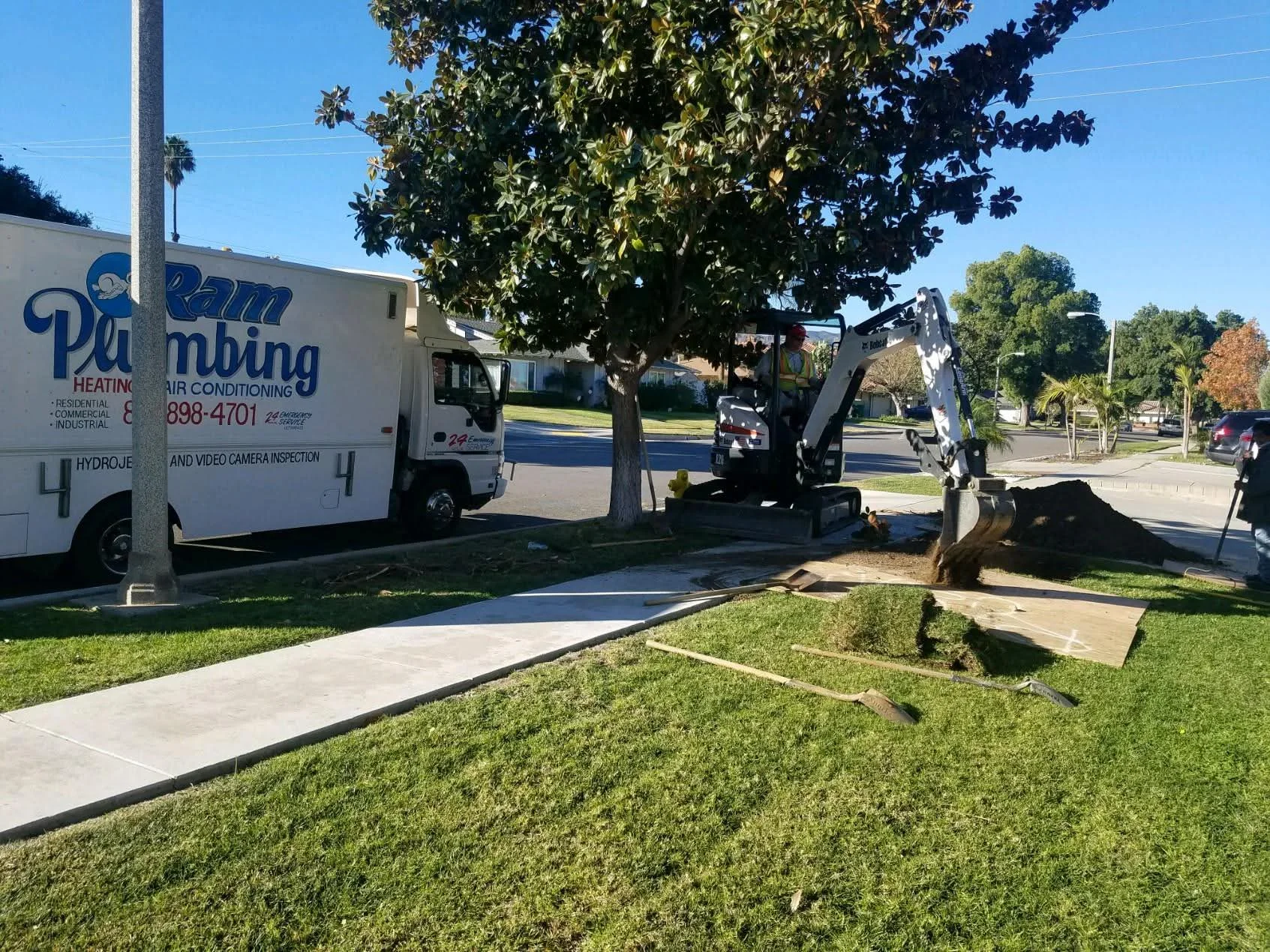 Mini excavator exposing underground sewer line with concrete and soil excavation in residential yard