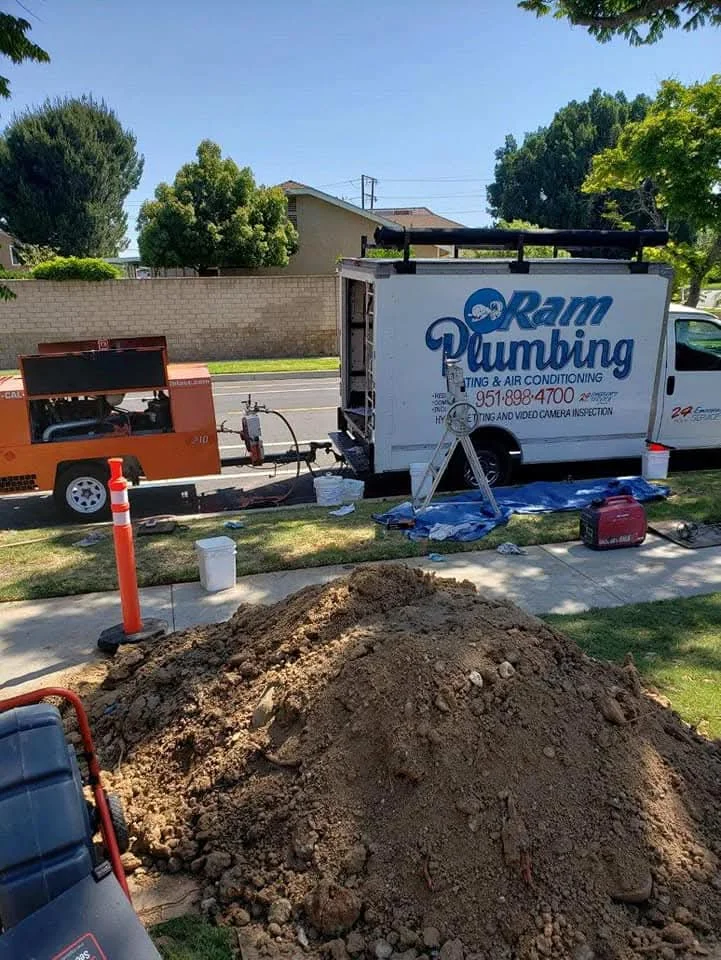 Excavated soil pile at residential property with plumbing service truck and equipment staged nearby