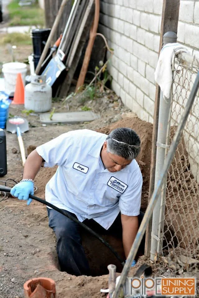 Plumber installing black perforated drain pipe along concrete block foundation with excavated soil