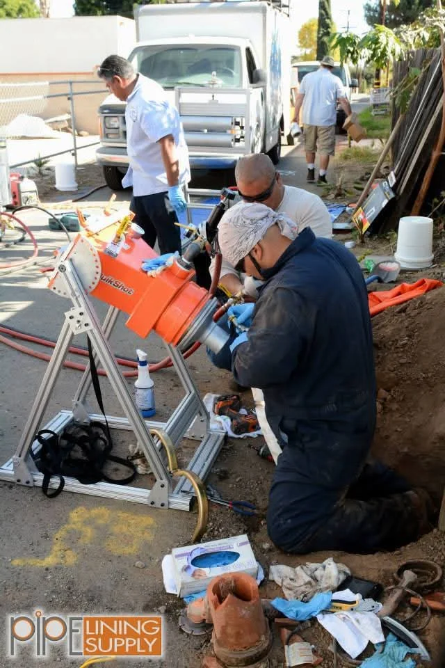 Crew operating orange trencher to install underground plumbing lines in excavated trench