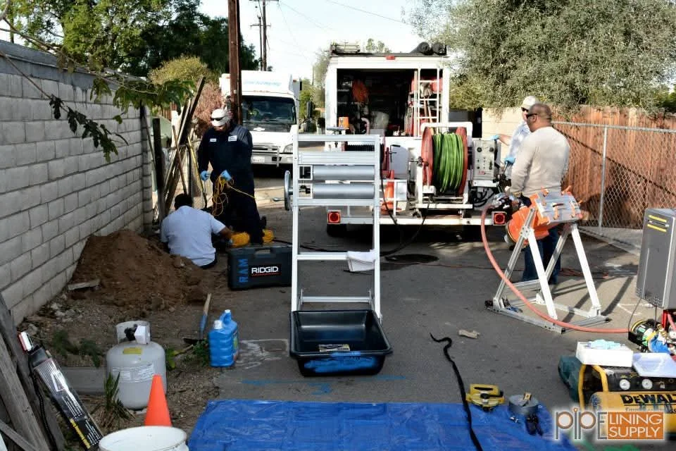Sewer line excavation with pipe-laying equipment, cable reel, and professional crew in residential backyard