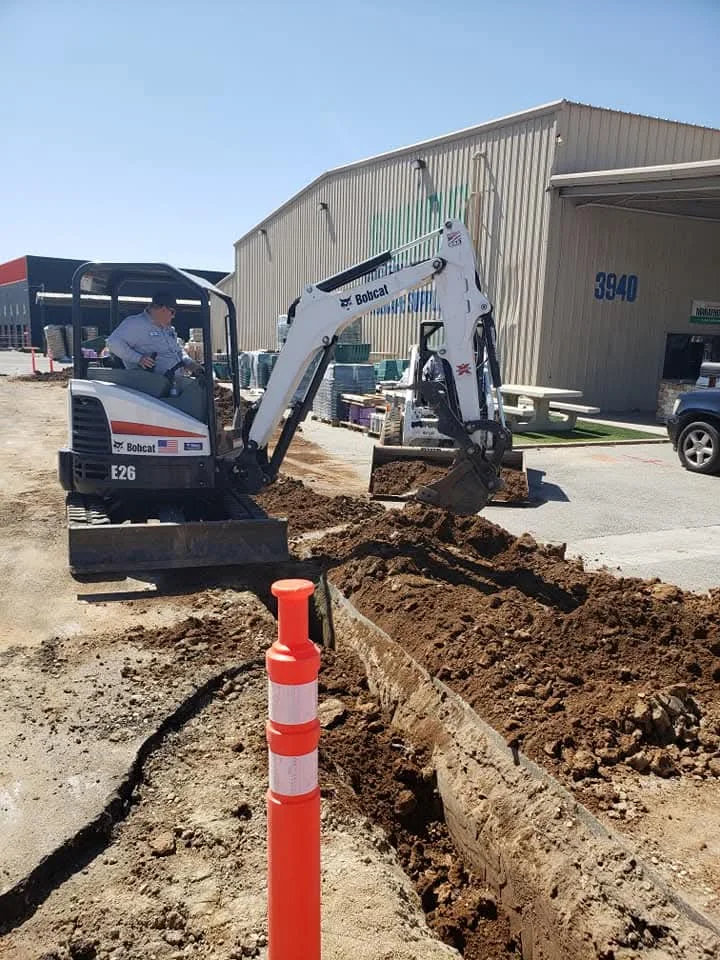 Bobcat E26 excavator digging trench for underground plumbing access at commercial site